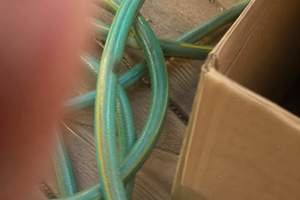A blurred photograph of a garden hose, partly obscured by a thumb